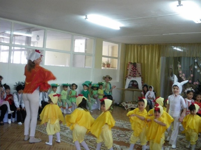Children in yellow and green, standing in a circle with an adult in white and red