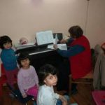 Baba sitting at a piano, looking away, with three children looking at the camera